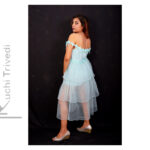 Woman in a layered light blue dress posing against a black backdrop.