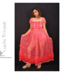 Woman in a vibrant orange-pink traditional dress posing against a dark background.