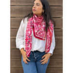 Woman wearing a white blouse, blue jeans, and a red patterned scarf.