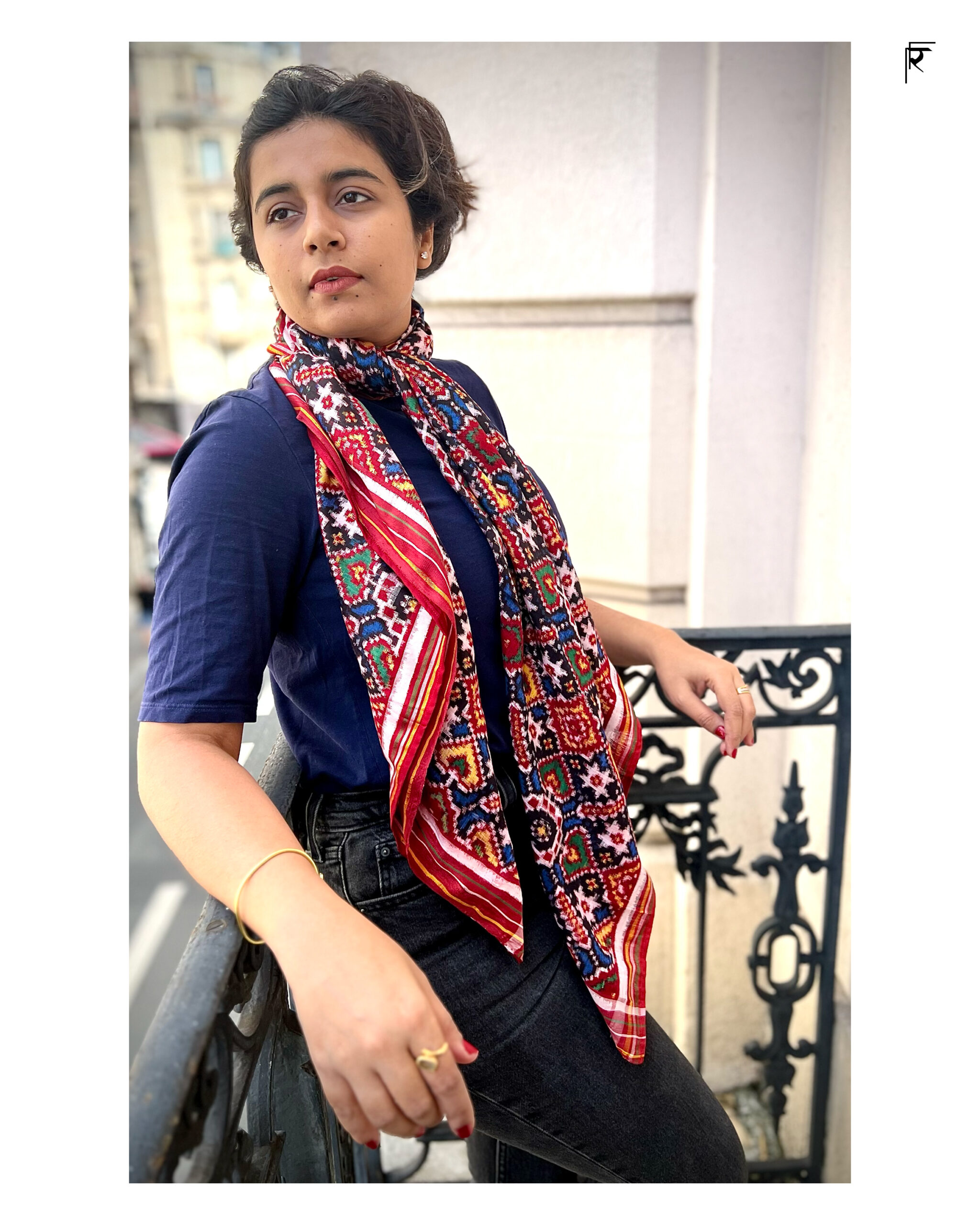 Woman wearing a colorful scarf and navy blue top, sitting outdoors.